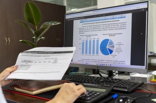 Pessoa em mesa de escritório analisando relatório financeiro com gráficos na tela do computador