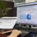 Pessoa em mesa de escritório analisando relatório financeiro com gráficos na tela do computador